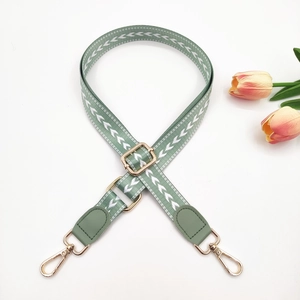 Close-up of adjustable light green woven strap with white arrow pattern and gold metal hooks