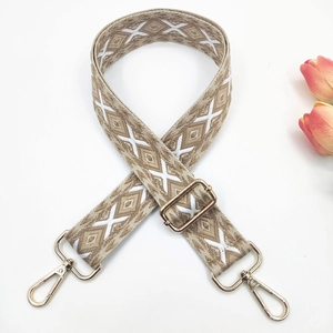 Close-up of beige ethnic embroidered bag strap with white geometric patterns and gold clips
