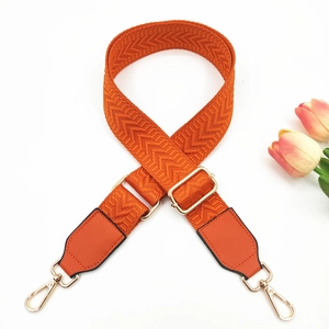 Detail of orange herringbone woven bag strap with PU leather ends and gold metal buckles