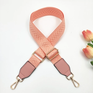 Close-up of adjustable pink-orange geometric woven bag strap with gold metal hooks