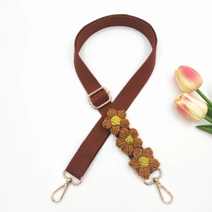 Detail of handcrafted crochet daisy flowers on a brown woven bag strap with gold lobster clasps