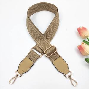 Macro detail of khaki arrow pattern woven bag strap with polished gold-toned metal buckles