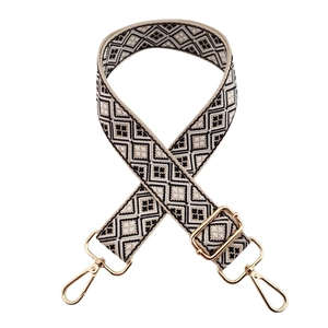 Close-up of wide woven bag strap with geometric jacquard pattern and gold metal hooks