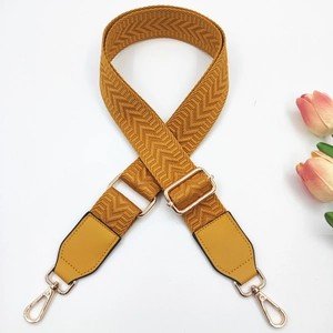 Macro detail of mustard yellow chevron woven bag strap with golden metal hooks and leather