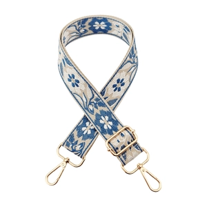 Detail view of ethnic floral embroidery on a wide shoulder strap with golden metal hardware