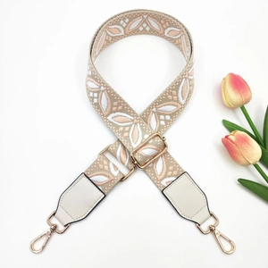 Detail of floral jacquard embroidered wide bag strap with gold metal hooks and leather trim