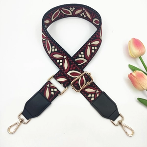 Close-up of ethnic jacquard purse strap with red leaf pattern and gold metal hardware