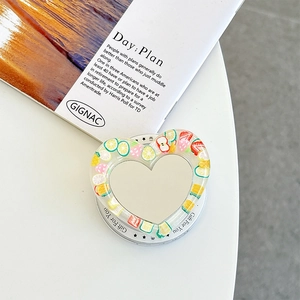 Macro detail of heart-shaped phone grip featuring resin fruit slices and a vanity mirror