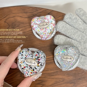 Sparkly glitter heart-shaped expanding phone grip with handmade metal logo on wood background