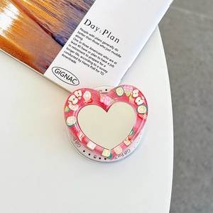Close-up of heart-shaped phone grip with red resin, fruit glitter, and integrated makeup mirror
