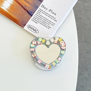 Detail of heart-shaped phone grip featuring mirror surface and colorful fruit charms
