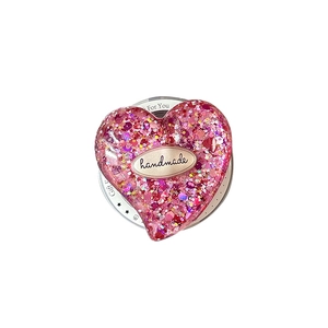 Pink heart-shaped glitter phone grip with handmade gold logo on a clean white background
