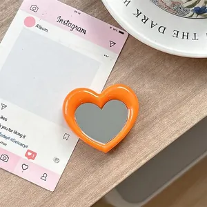 Detail van hartvormige oranje telefoonhouder met spiegel op een houten tafelblad