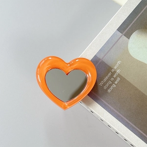 Detail of an orange heart-shaped phone grip mirror on a stylish magazine background