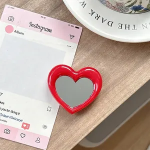 Detail van de rode hartvormige telefoonhouder met spiegel op een houten oppervlak