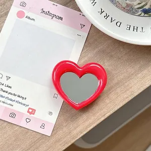 Detail van een rode hartvormige inklapbare telefoonspiegel op een houten bureau