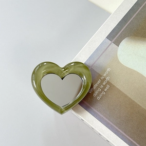 Macro detail of heart-shaped sage green marble phone mirror stand on lifestyle magazine