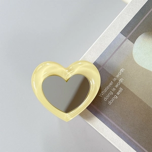 Macro shot of heart-shaped phone grip with yellow acrylic frame and integrated makeup mirror