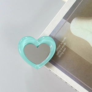 Detail of mint green heart-shaped phone grip mirror on a minimalist magazine background