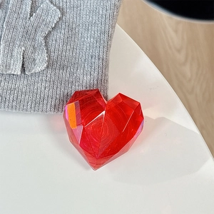 Detail of red 3D faceted crystal heart phone grip on white surface with knit texture