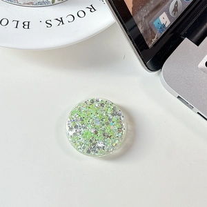 Close-up of a circular phone grip with green glitter sequins on a white desk