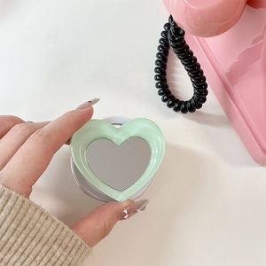 Detail of mint green heart-shaped phone grip with built-in mirror and compact design