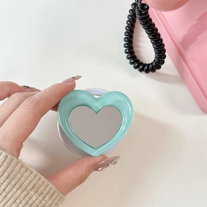 Macro view of mint green heart-shaped phone grip with built-in mirror for makeup
