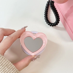 Pink heart-shaped magnetic phone grip with mirror finish held against retro background