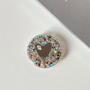 Close-up of a round glittery phone griptok with a heart mirror and mi ne. text
