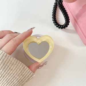 Close-up of heart-shaped magnetic phone grip with integrated mirror on white desk