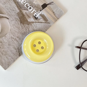 Minimalist candy yellow button phone stand shown with stylish glasses and magazine lifestyle setup