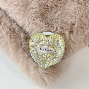 Detail of a heart-shaped glitter phone grip with handmade tag on a plush background