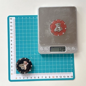 Detail shot of rhinestone bear phone grips showing a 12.0g weight on a digital scale