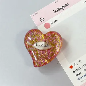 Dettaglio di un supporto per telefono a cuore con glitter rosa, oro e etichetta handmade