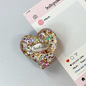 Dettaglio macro di un supporto per telefono a cuore in resina con glitter e placca metallica