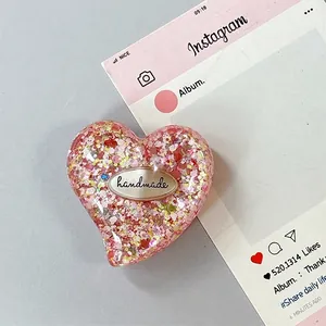 Dettaglio del supporto per telefono a cuore glitterato con scritta handmade e paillettes