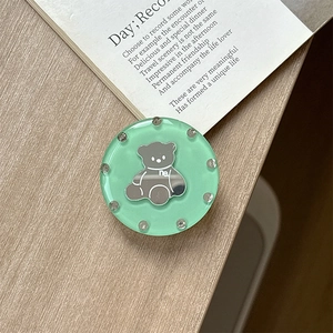 Detail shot of a light green resin bear phone grip mirror with rhinestones on a desk