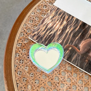 Detail view of a heart-shaped holographic phone grip mirror on a woven rattan surface