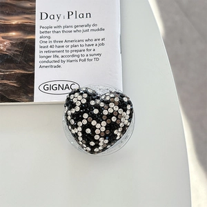 Close-up of heart-shaped phone grip with black and white rhinestones on white desk