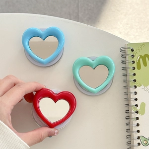 Magnetic heart-shaped phone mirror stands in blue, mint green, and red on a white desk