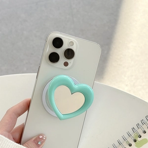 Close-up of mint green heart-shaped phone grip with a built-in makeup mirror on white phone