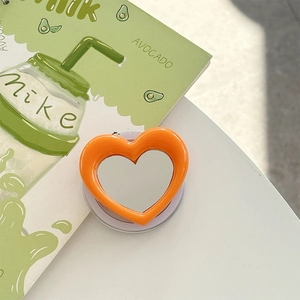 Macro view of orange heart-shaped phone grip with built-in mirror and avocado decor