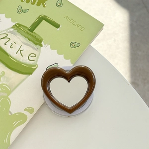 Macro detail of a brown heart-shaped phone grip mirror on a stylish desktop setup