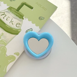 Close-up of blue heart-shaped phone grip with built-in makeup mirror on white desk