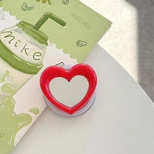 Detail of red heart-shaped magnetic phone grip with a compact mirror on white desk