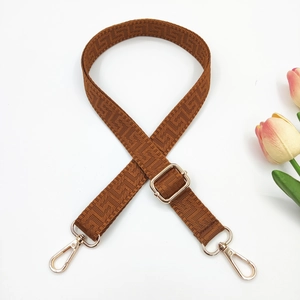 Detail of adjustable brown woven shoulder strap with gold hooks and geometric pattern