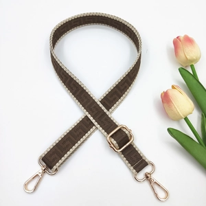 Detail of adjustable geometric pattern shoulder strap with gold metal hardware on white background