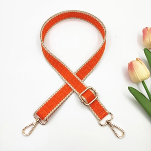 Detail of adjustable orange and beige woven bag strap with golden metal swivel hooks