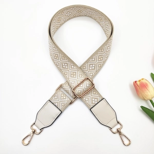 Detail of adjustable geometric jacquard bag strap with gold metal hooks and white leather