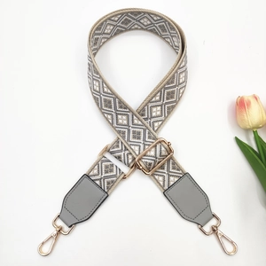 Close-up of geometric jacquard bag strap with grey leather ends and gold metal hooks